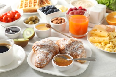 Tasty breakfast. Croissants, jam, coffee and other food on light table, closeup