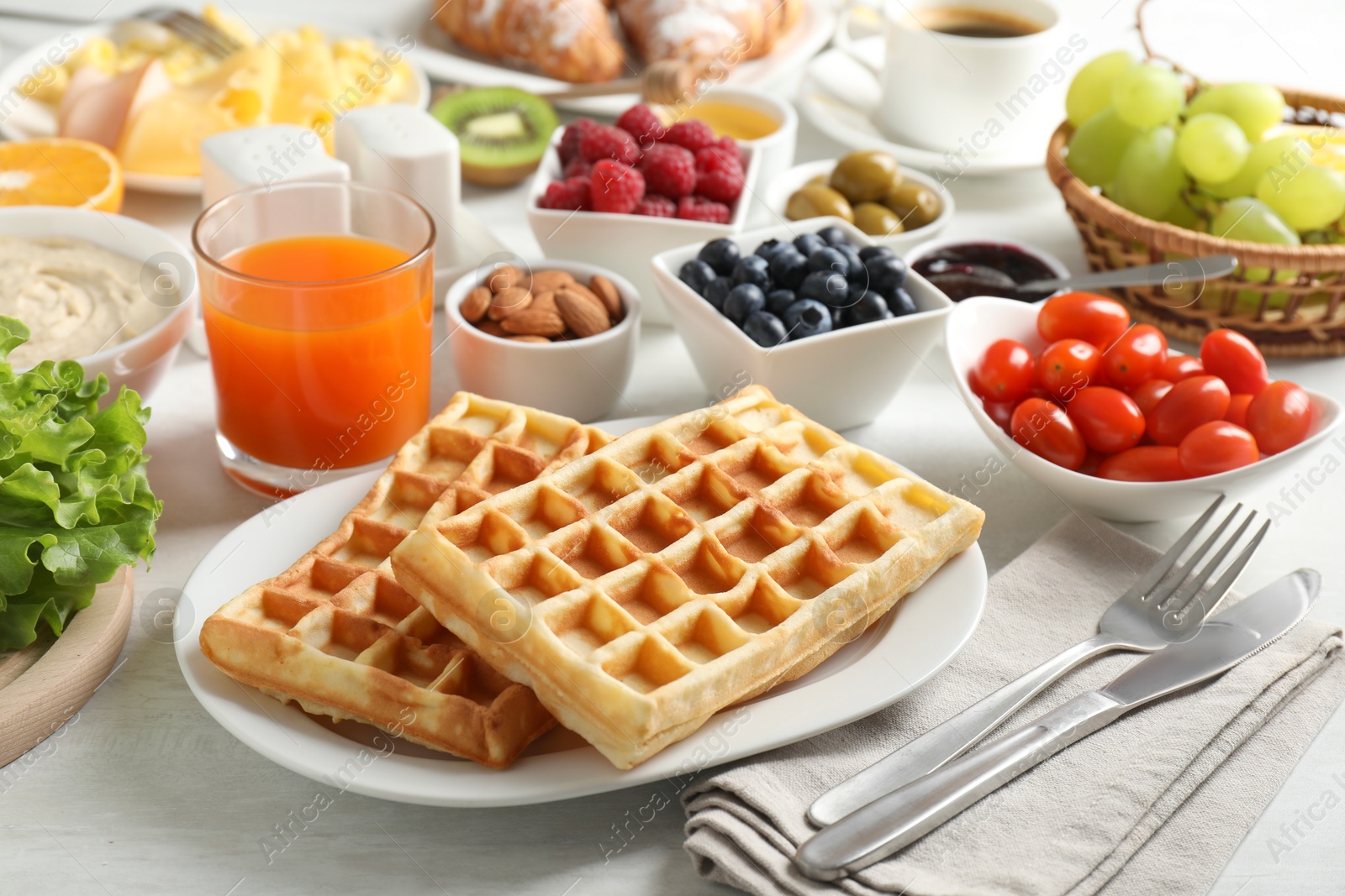 Photo of Tasty breakfast. Belgian waffles, orange juice and other food on light wooden table, closeup