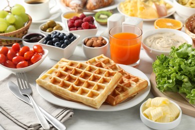 Photo of Tasty breakfast. Belgian waffles, orange juice, butter and other food on light wooden table, closeup