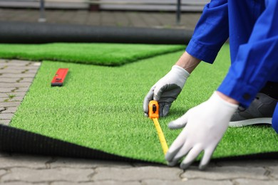 Photo of Man in uniform installing artificial turf outdoors, closeup