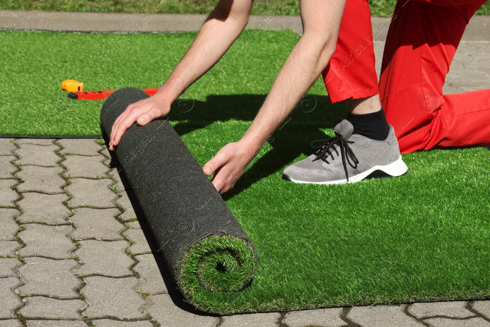 Photo of Man in uniform installing artificial turf outdoors, closeup