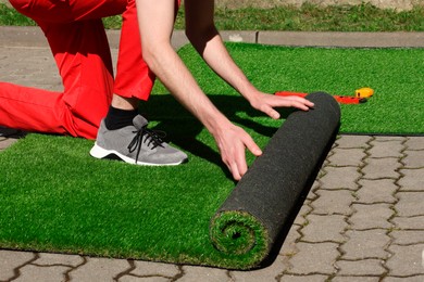 Man in uniform installing artificial turf outdoors, closeup