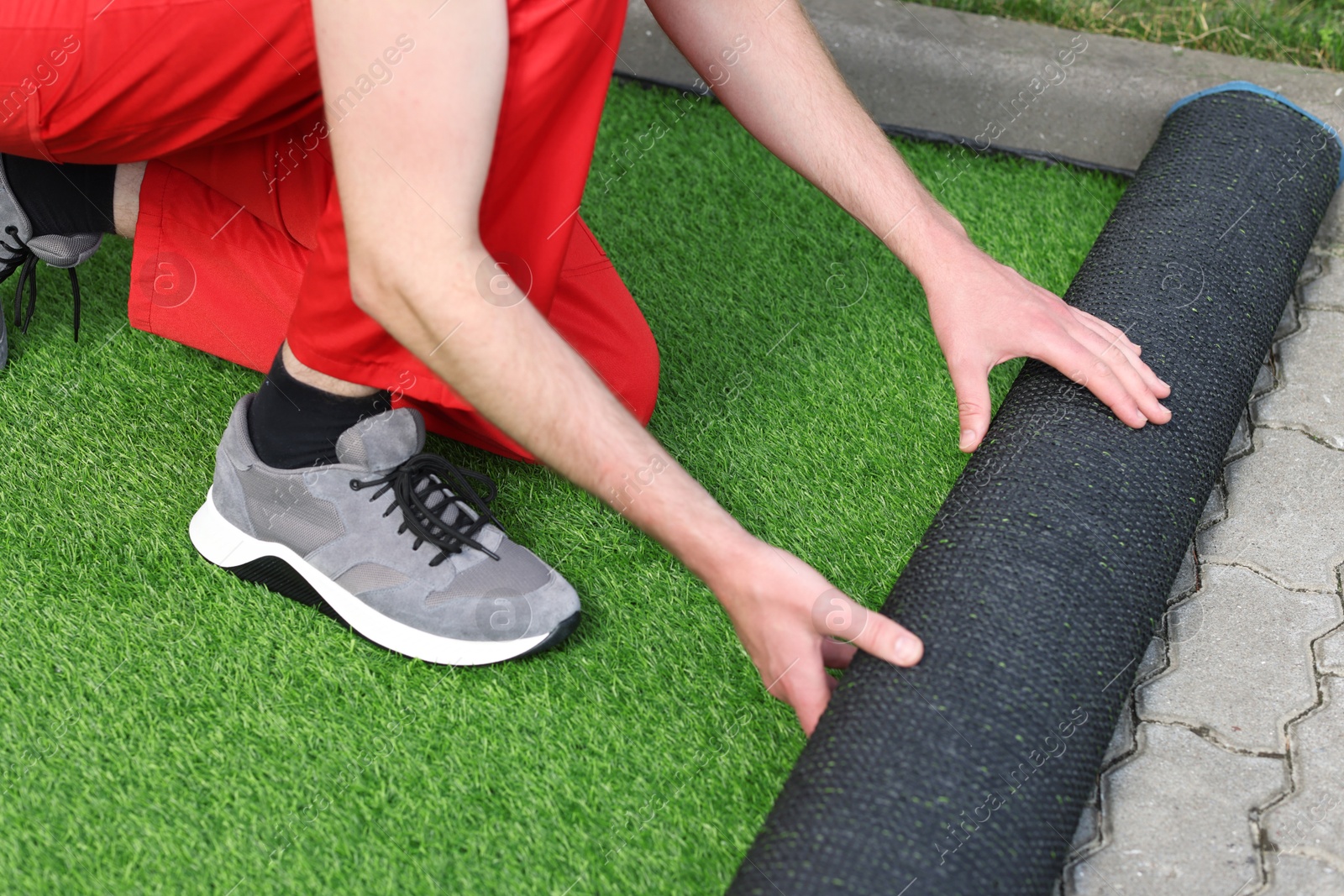 Photo of Man in uniform installing artificial turf outdoors, closeup