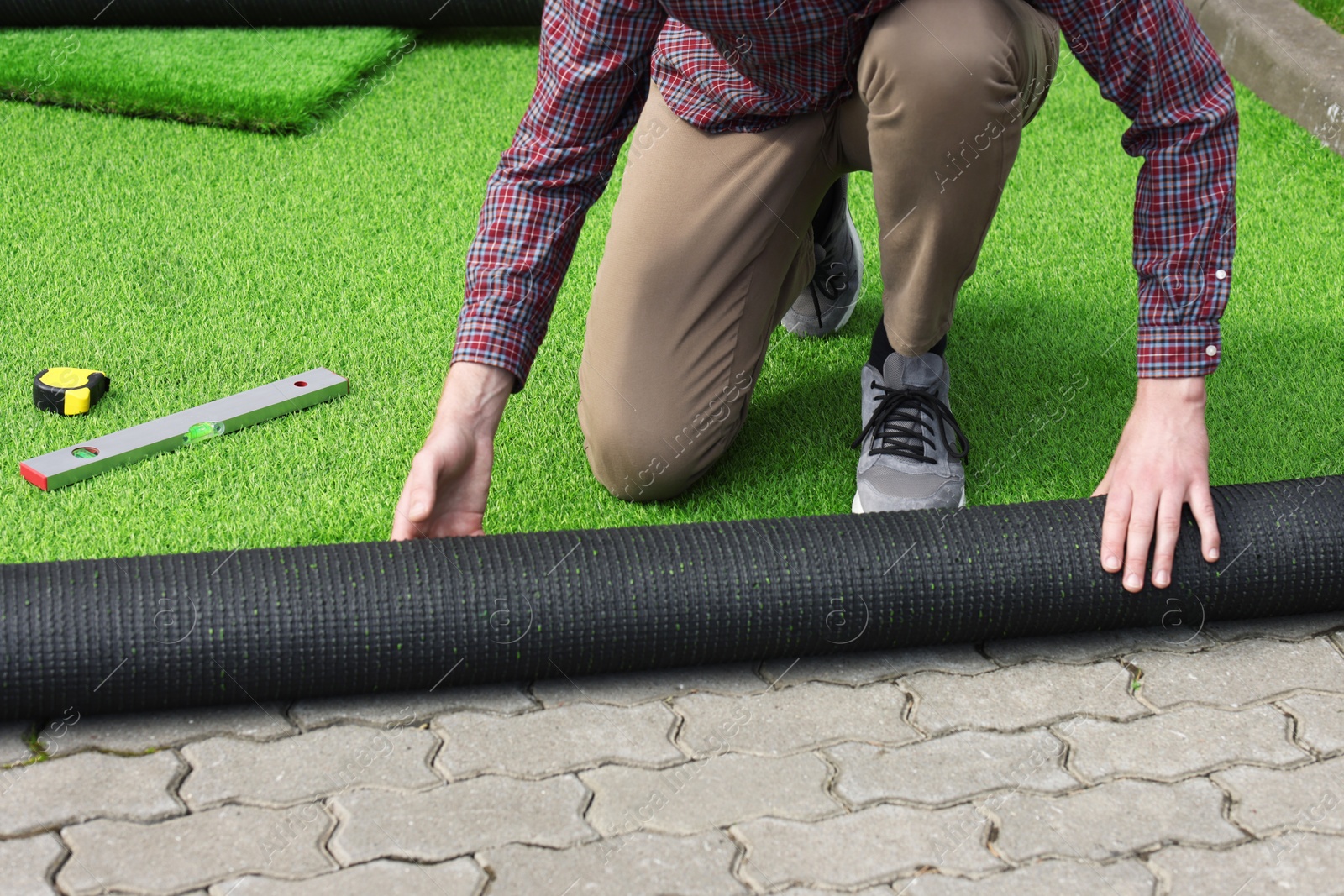 Photo of Man installing artificial turf outdoors, closeup view