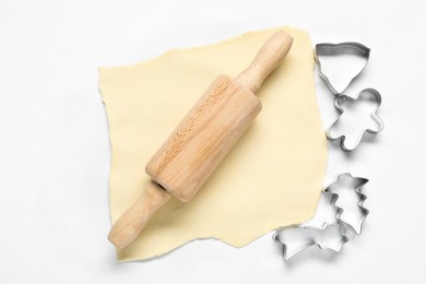 Raw dough, rolling pin and cookie cutters on white background, flat lay