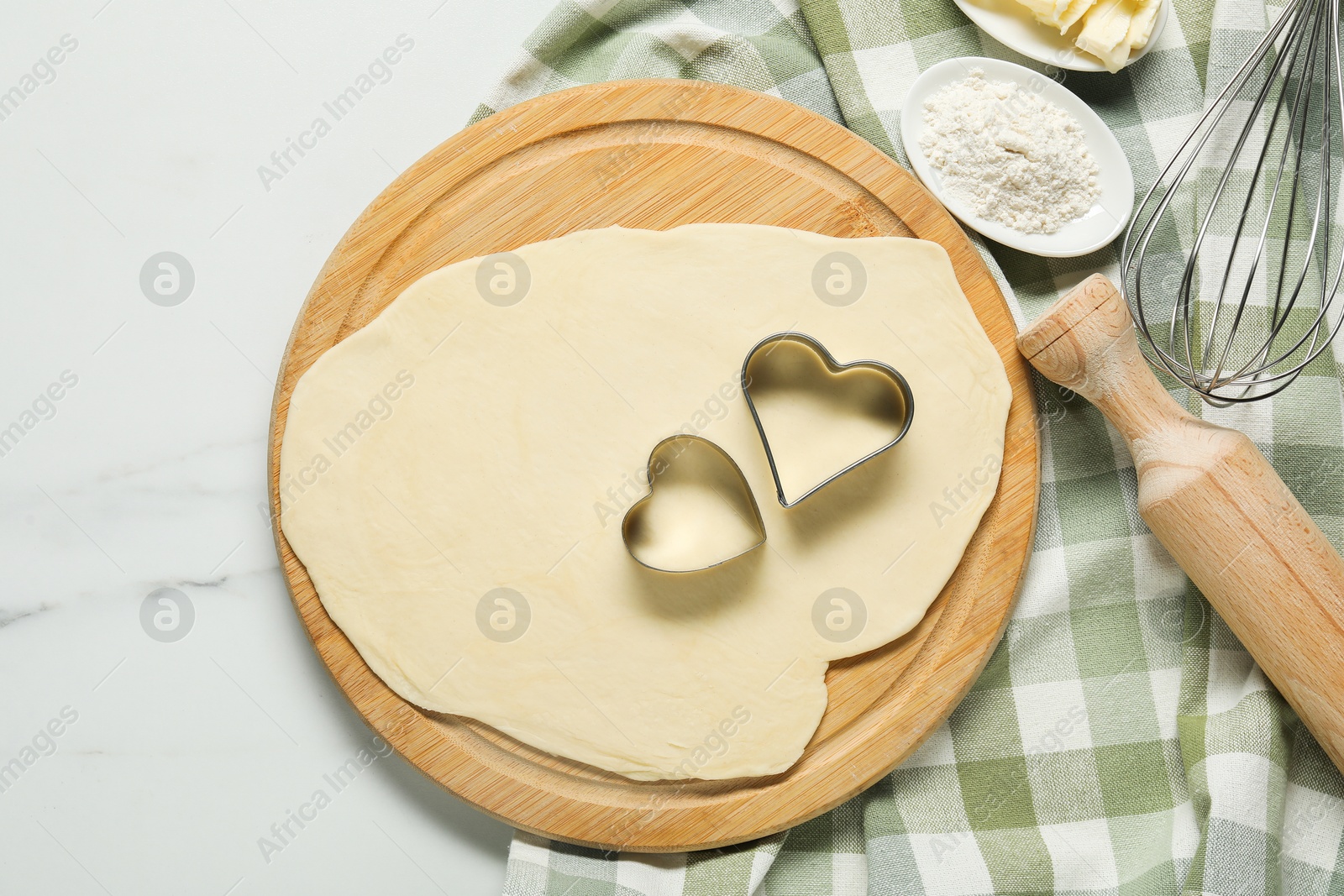 Photo of Raw dough, cookie cutters, flour, whisk and rolling pin on white marble table, top view