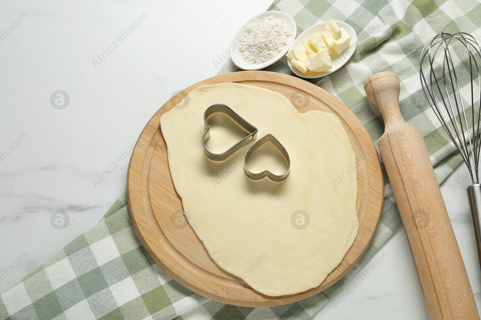 Photo of Raw dough, cookie cutters, flour, butter, whisk and rolling pin on white marble table, flat lay