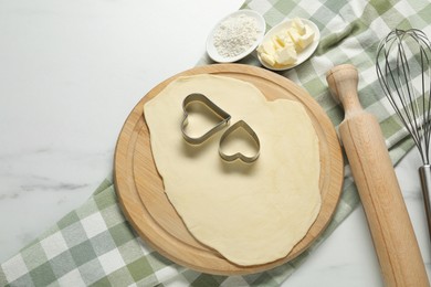 Photo of Raw dough, cookie cutters, flour, butter, whisk and rolling pin on white marble table, flat lay