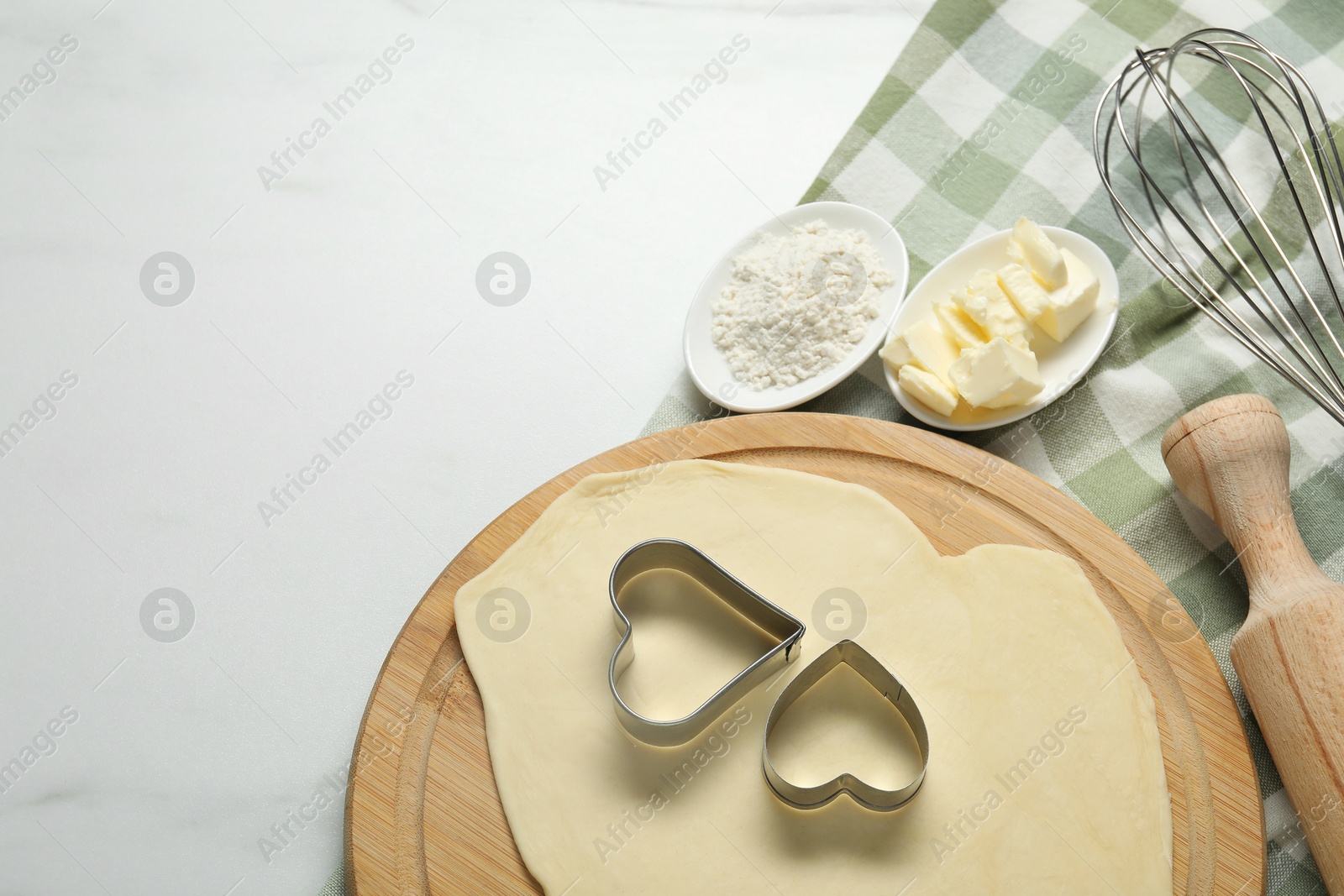 Photo of Raw dough, cookie cutters, flour, butter, whisk and rolling pin on white marble table, top view. Space for text