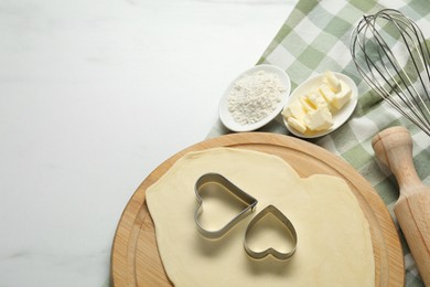 Raw dough, cookie cutters, flour, butter, whisk and rolling pin on white marble table, top view. Space for text