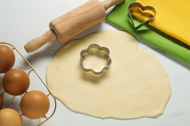 Raw dough, cookie cutters, eggs, napkins and rolling pin on white marble table, above view