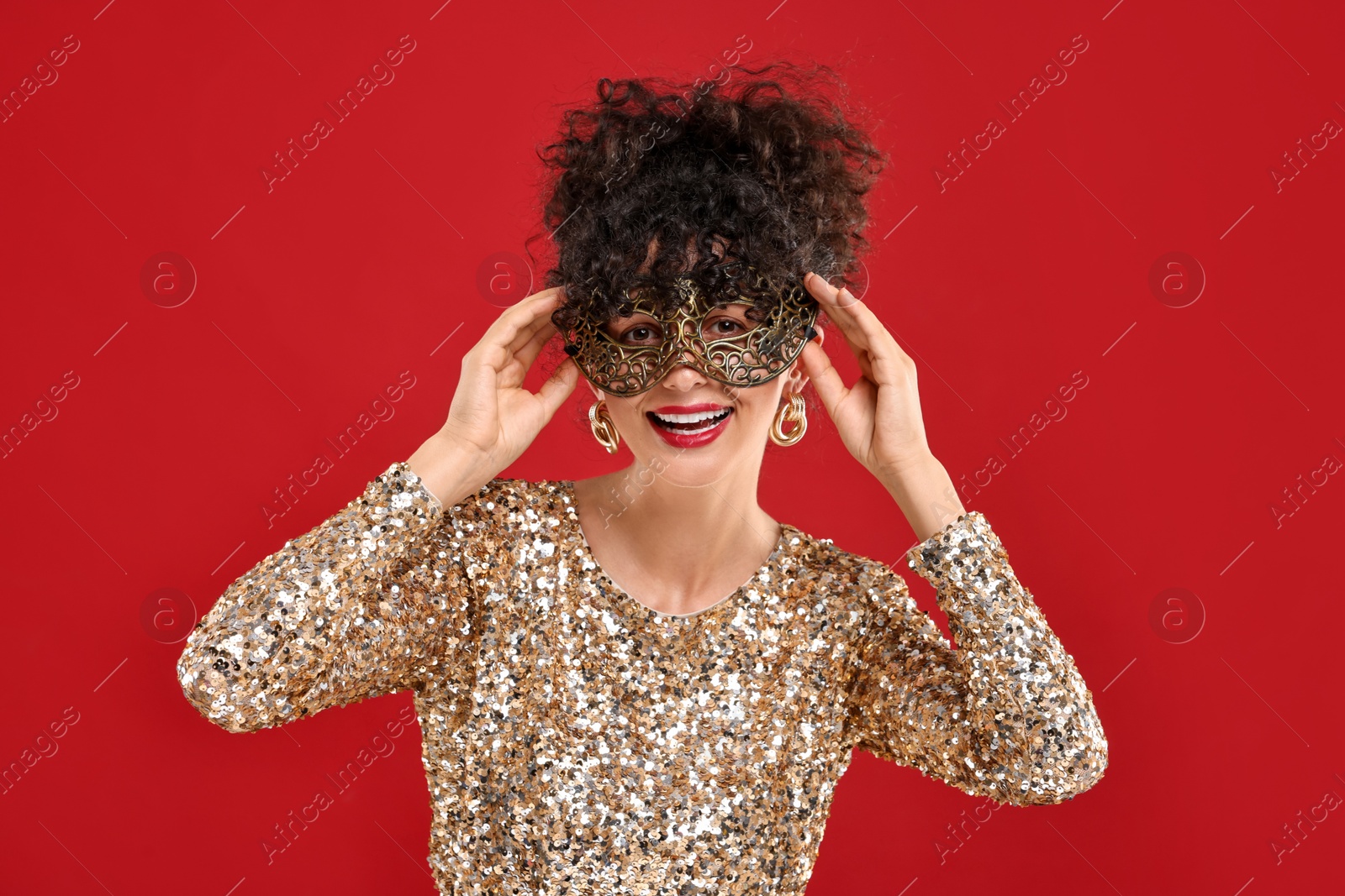 Photo of Smiling young woman wearing carnival mask on red background