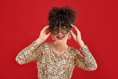 Smiling young woman wearing carnival mask on red background