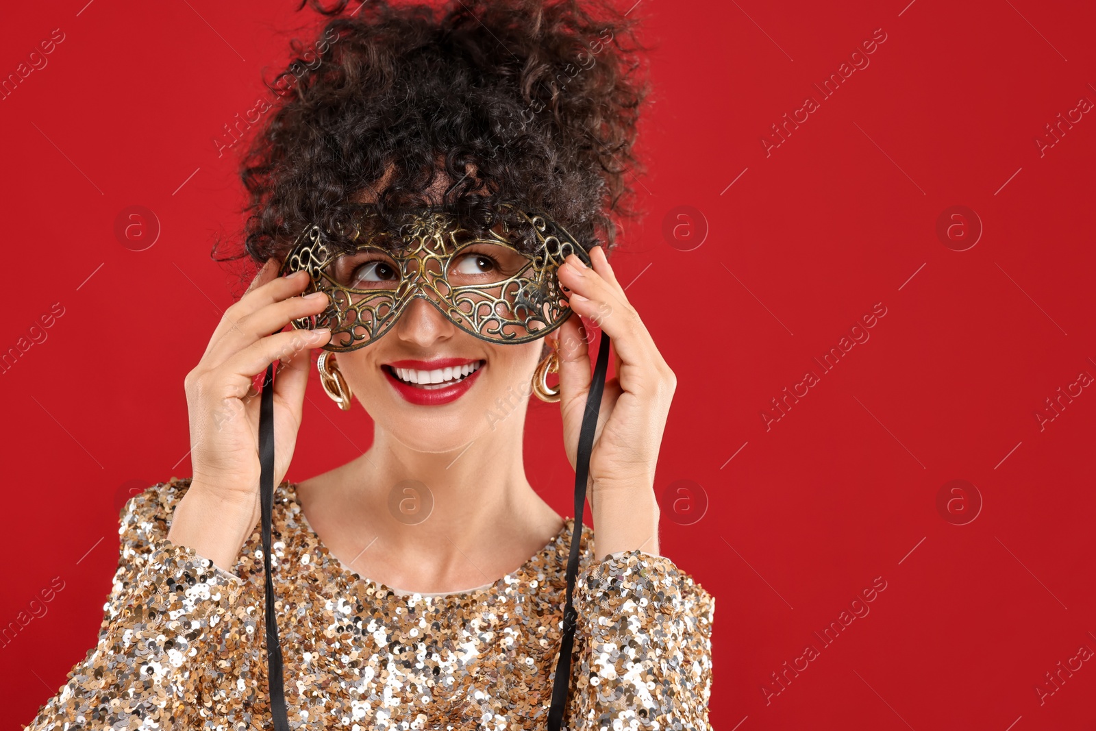 Photo of Smiling young woman wearing carnival mask on red background, space for text