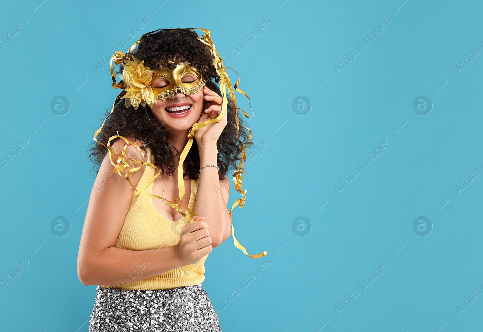 Photo of Happy young woman wearing carnival mask and tinsel on light blue background, space for text