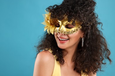 Happy young woman wearing carnival mask on light blue background