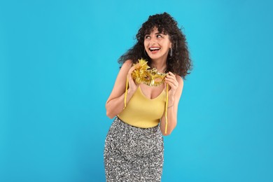 Happy young woman with carnival mask on light blue background