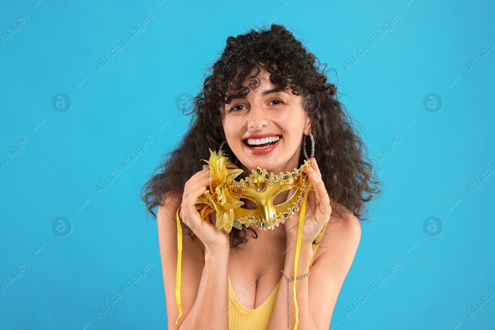 Photo of Happy young woman with carnival mask on light blue background