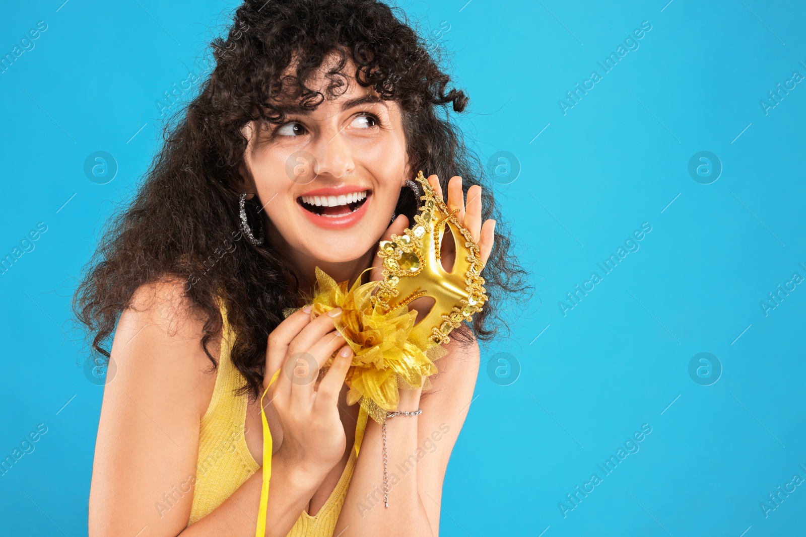 Photo of Happy young woman with carnival mask on light blue background, space for text