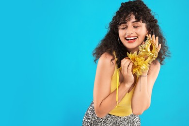 Happy young woman with carnival mask on light blue background, space for text