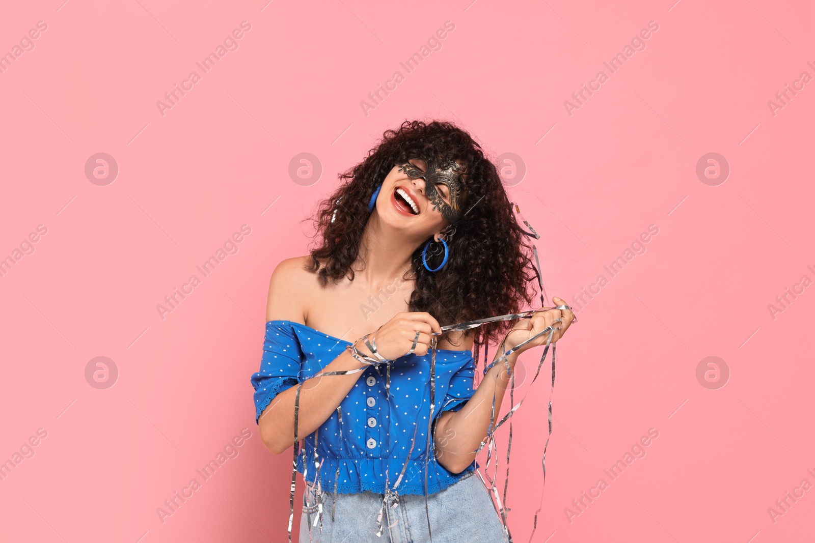 Photo of Happy young woman wearing carnival mask and tinsel on pink background