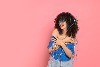 Photo of Happy young woman wearing carnival mask and tinsel on pink background, space for text