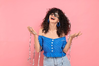 Photo of Happy young woman wearing carnival mask and tinsel on pink background