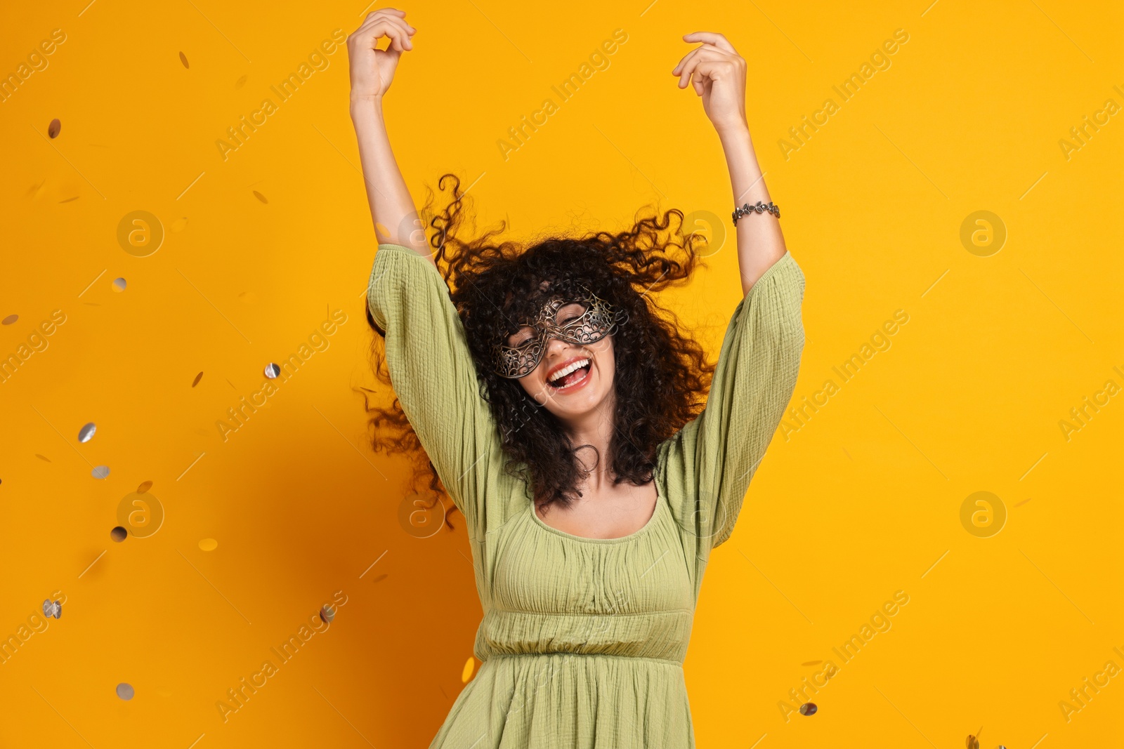 Photo of Happy young woman wearing carnival mask and confetti on yellow background