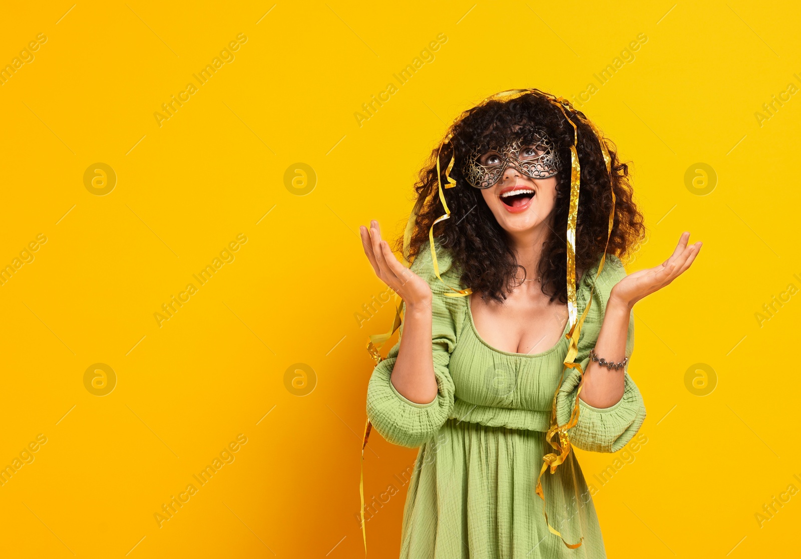 Photo of Happy young woman wearing carnival mask and tinsel on yellow background, space for text