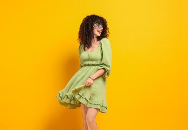 Photo of Happy young woman wearing carnival mask on yellow background