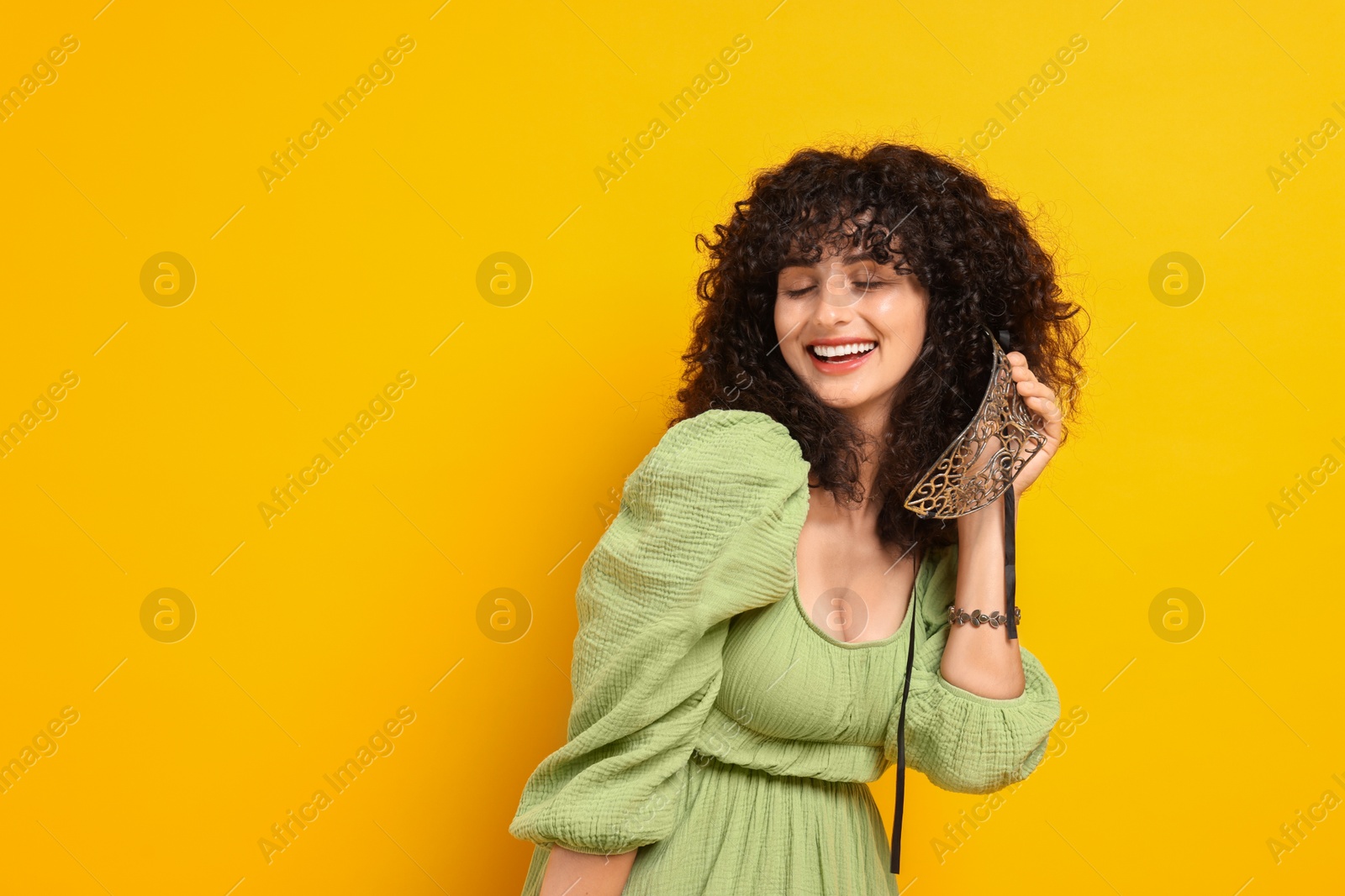 Photo of Smiling young woman with carnival mask on yellow background, space for text