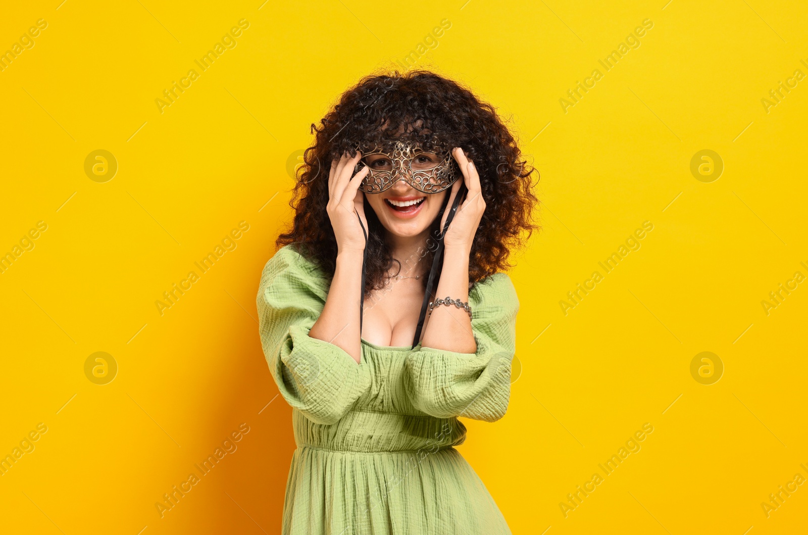 Photo of Happy young woman wearing carnival mask on yellow background