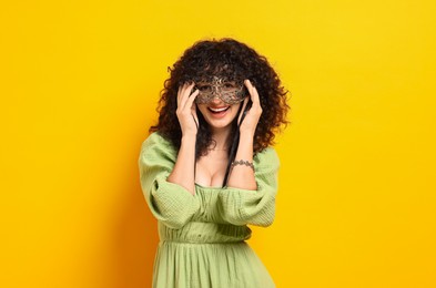 Happy young woman wearing carnival mask on yellow background