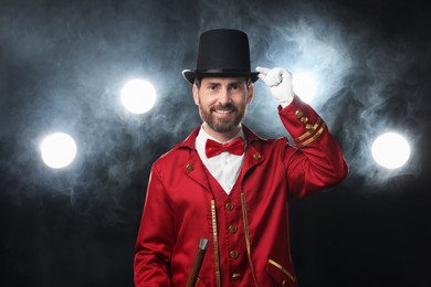 Photo of Portrait of showman in red costume, cane and hat on black background with spotlights and smoke