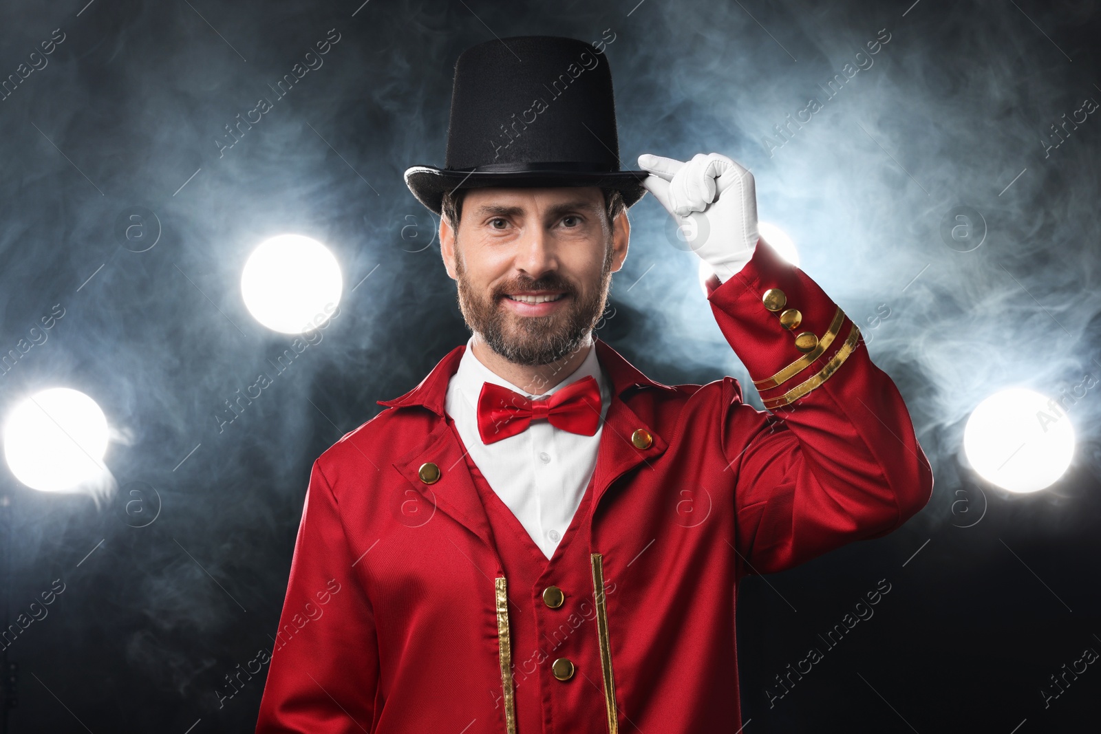 Photo of Portrait of showman in red costume, cane and hat on black background with spotlights and smoke