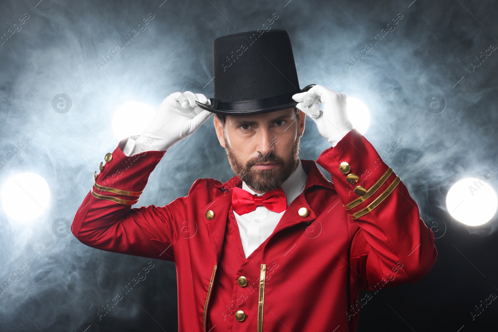 Photo of Portrait of showman in red costume and hat on black background with spotlights and smoke