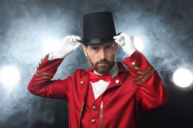 Photo of Portrait of showman in red costume and hat on black background with spotlights and smoke