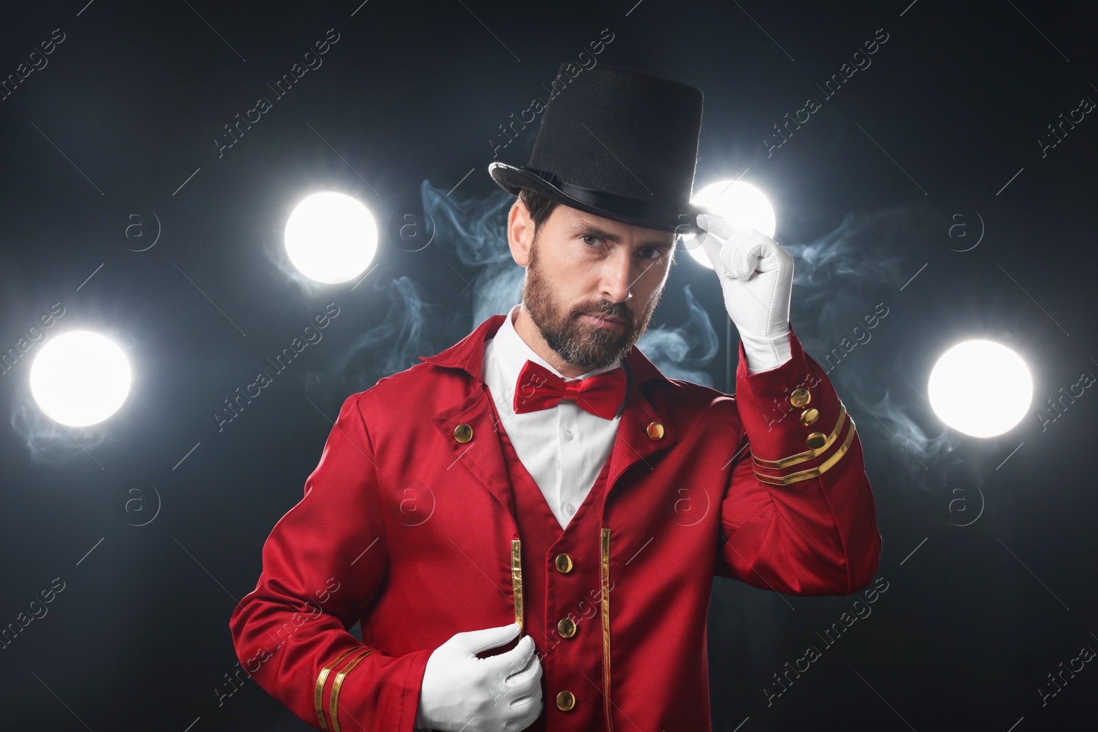 Photo of Portrait of showman in red costume and hat on black background with spotlights and smoke