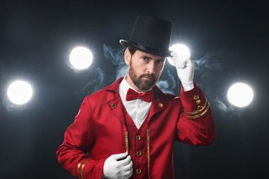 Photo of Portrait of showman in red costume and hat on black background with spotlights and smoke