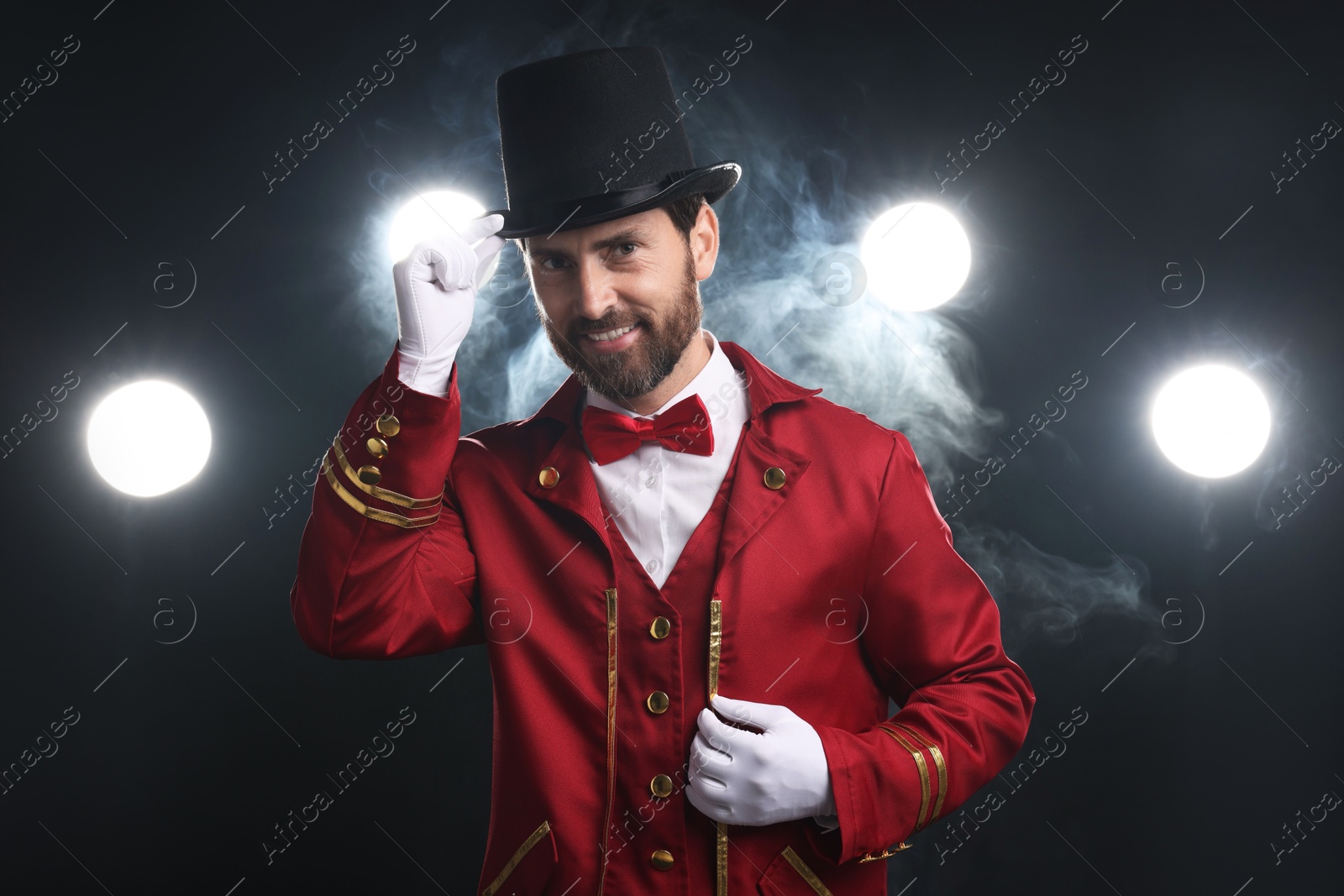 Photo of Portrait of showman in red costume and hat on black background with spotlights and smoke