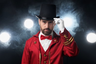 Photo of Portrait of showman in red costume and hat on black background with spotlights and smoke