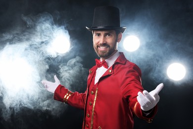 Photo of Portrait of showman in red costume and hat on black background with spotlights and smoke