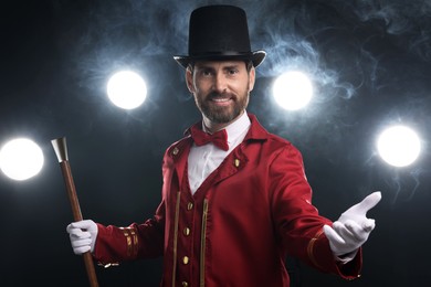 Photo of Portrait of showman in red costume, cane and hat on black background with spotlights and smoke