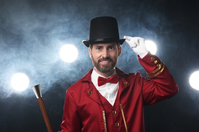 Photo of Portrait of showman in red costume, cane and hat on black background with spotlights and smoke