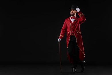 Portrait of showman in red costume and hat on black background, space for text