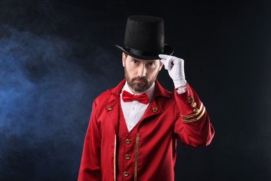 Photo of Portrait of showman in red costume and hat on black background with smoke