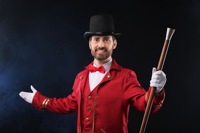 Portrait of showman in red costume and hat on black background with smoke