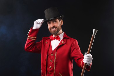 Photo of Portrait of showman in red costume and hat on black background with smoke