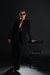 Photo of Beautiful woman in stylish suit near chair on black background