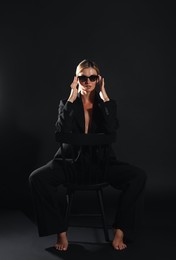 Beautiful woman in stylish suit sitting on chair against black background